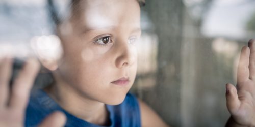 one sad little boy standing near the window at the day time. Concept of sorrow.