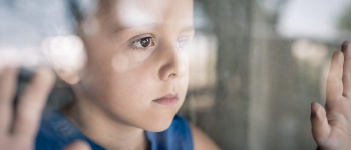 one sad little boy standing near the window at the day time. Concept of sorrow.