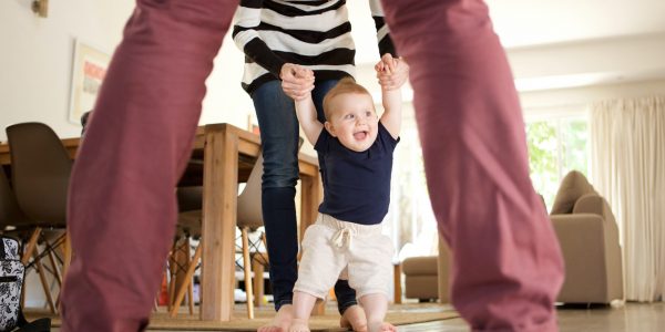 Portrait of cute baby boy learning to walk with mother and father at home