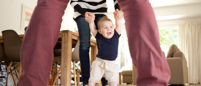 Portrait of cute baby boy learning to walk with mother and father at home