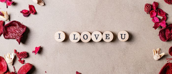 Word love made with wooden circle stamps with flowers over brown texture background. Top view, flat lay. Copy space