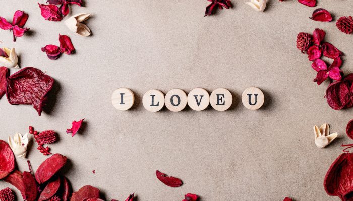 Word love made with wooden circle stamps with flowers over brown texture background. Top view, flat lay. Copy space
